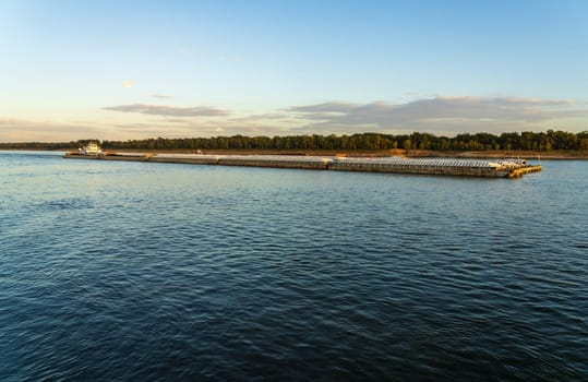 Large river barge loaded with grain sailing down Mississippi river near Natchez at dusk