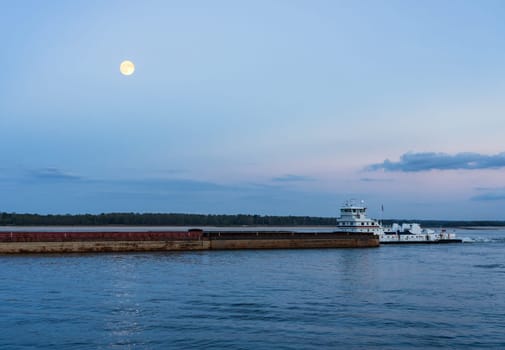 Large river barge loaded with grain sailing down Mississippi river near Natchez at dusk