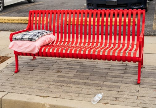 Red street bench with folded blanket and pillow as concept for homelessness in Baton Rouge, the state capital of Louisiana
