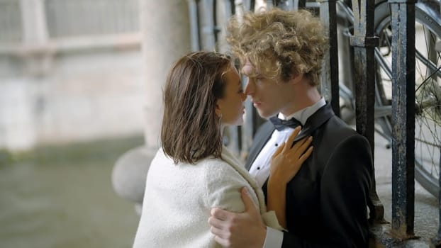 Passionate bride and groom embracing by the iron gate. Action. Sexy young man and woman in suit and white dress in windy weather