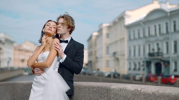 Young bride and groom posing in a city on a windy day. Action. Young woman in white dress and a man in suit in the city outdoors