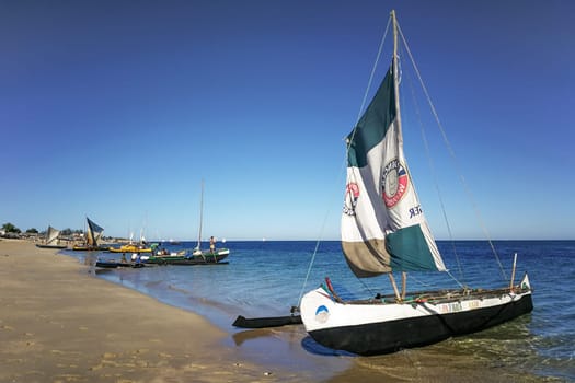 Anakao, Madagascar - May 03, 2019: Fisherman piroga (small fishing boat with sail) waiting at the coast on sunny day, more ships in background