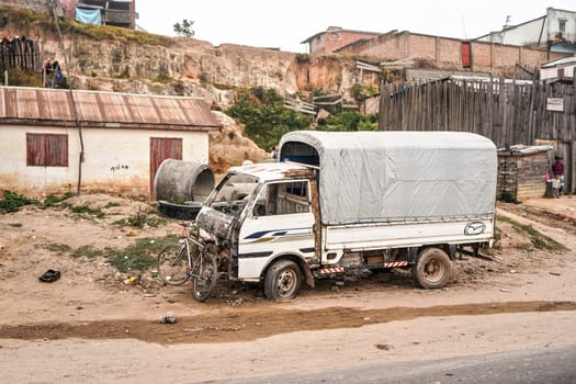 Antananarivo, Madagascar - May 07, 2019: Bicycle leaning on broken truck hood, near main road, garbage on ground - typical scene - as most parts of Madagascar except capital centre are very poor