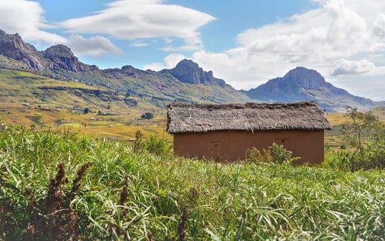 Typcial landscape at Andringitra National Park, Madagascar on sunny day. Rocky mountains with rice fields under at distance, small clay house with stray roof in foreground