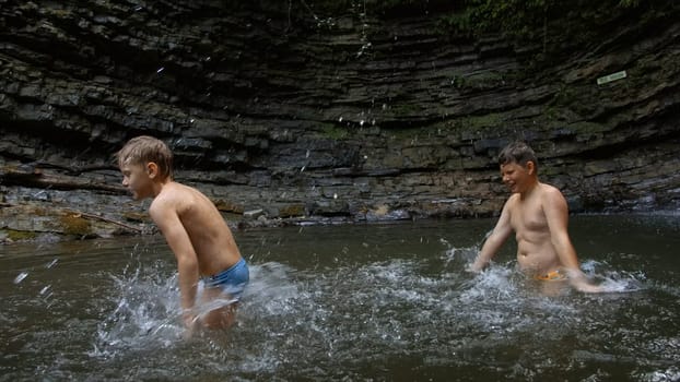 Young boys bathing in a small lake within the mountain. Creative. Little boys splashing cold water