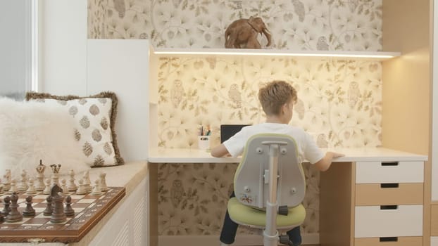 Interior of children's room with boy sitting at table. Creative. Boy is studying at desk. Children's room of smart boy studying at table.