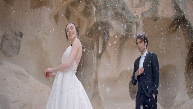 Photo shoot of the newlyweds in nature. Action. A cute couple in wedding costumes in the mountains posing for a photo session and it's snowing. High quality 4k footage