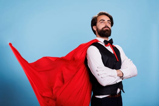Powerful superhero wears red cape and feeling strong to save citizens, posing against blue background. Determined leader in formal clothes acting confident, fantasy cartoon concept.
