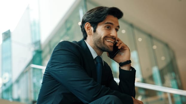 Smart business man calling phone to manager while discuss about business plan. Skilled executive manager talking to phone with blurred background. Successful investor smiling while sitting. Exultant.