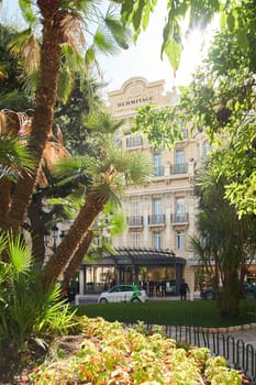 Monaco, Monte-Carlo, 09 November 2022: The Hotel Hermitage through flowers at sunny day, luxury life, building exterior of famous hotel, palm trees, sunshine, balcony. High quality photo