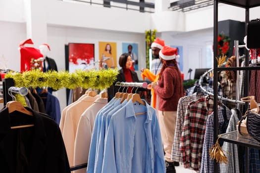 Retail workers showing jacket to woman in boutique, client shopping for new formal christmas attire in clothing store. Man and woman employees helping customer to choose perfect clothing items.