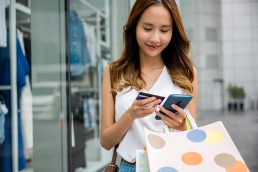 Connected consumer ,young woman using her smartphone to make purchases and stay connected while holding shopping bags and credit card. Technology and shopping at its finest