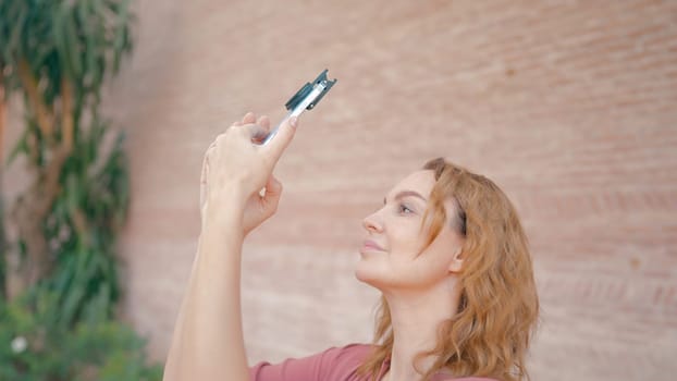 Beautiful woman takes pictures on phone. Action. Attractive woman on vacation takes pictures on phone with lens. Shooting on phone with professional lens on vacation.