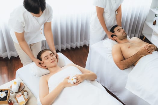 Caucasian couple enjoying relaxing anti-stress head massage and pampering facial beauty skin recreation leisure in dayspa modern light ambient at luxury resort or hotel spa salon. Quiescent
