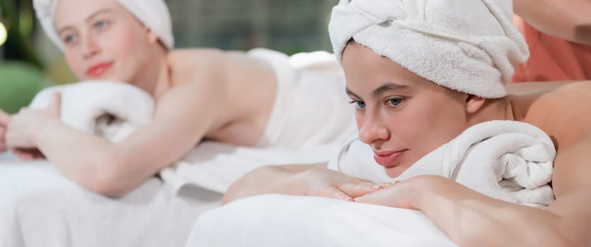 A portrait of a couple of a beautiful young caucasian woman with white towel rest on comfortable spa bed with relaxation while having body massage with professional masseur at spa salon.Tranquility.