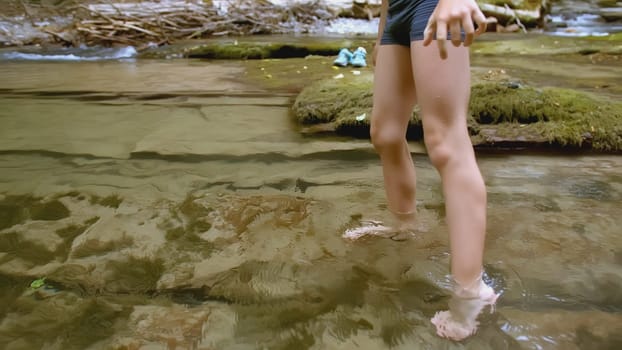 Boy walks in water in forest. Creative. Boy in swimming trunks walks on water in summer forest. Boy's feet walk on water in wild forest in summer. Summer hike in wild woodland.