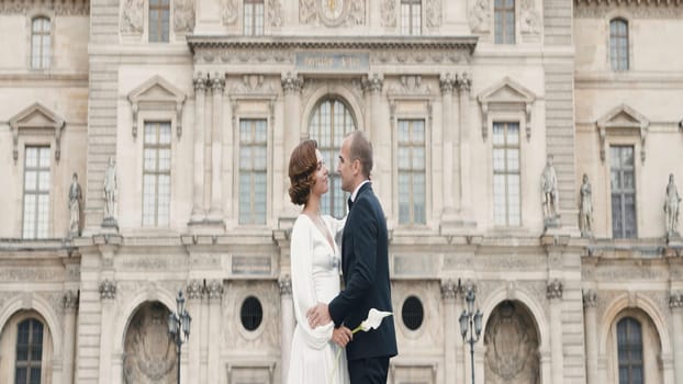 Adult couple in elegant outfits hugging. Action. Luxurious couple embraces in love on background of palace. Couple in love in elegant outfits on old square.