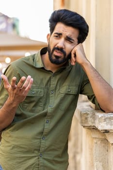 Sad unhappy indian man thinks over life concerns, suffers from unfair situation. Problem, feeling bad, annoyed, burnout grief. Frustrated depressed lonely arabian guy standing in city street. Vertical