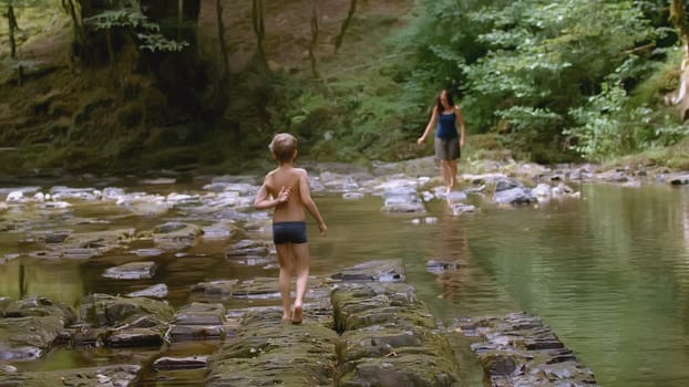 Woman and boy walk by river in forest. Creative. Mother and child walk in wild forest with river in summer. Family trip to wild forest in summer.