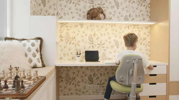 Interior of children's room with boy sitting at table. Creative. Boy is studying at desk. Children's room of smart boy studying at table.