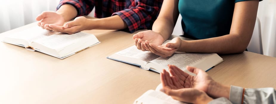 Cropped image of diversity people hand praying together at wooden church on bible book. Group of believer hold hand together faithfully. Concept of hope, religion, faith, god blessing. Burgeoning.