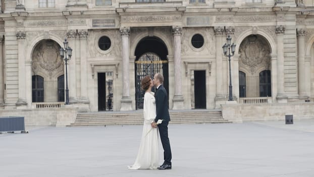 Couple kissing on background of ancient palace. Action. Beautiful view of kissing couple and palace. Couple in elegant outfits kissing in ancient city.