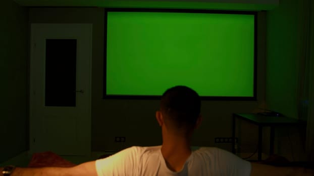 Viewing on a projector in a closed room. Media. A man looking into a green screen that is shown on a large screen. High quality 4k footage