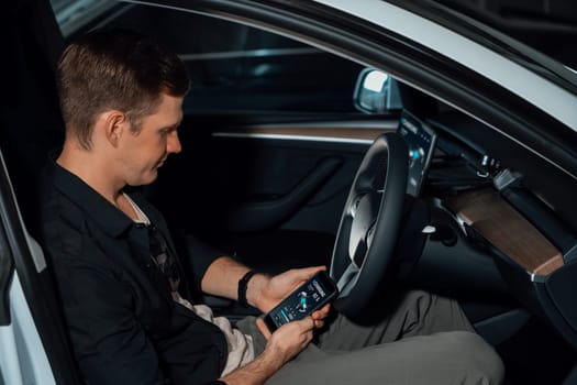 Electric car driver checks battery charging status, range and charging limit on app screen in the car. Smart technology device show EV car recharging data of electric storage in car battery innards.