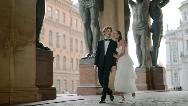 Beautiful newlyweds walking along European street. Action. Happy newlyweds are walking around city in wedding dresses. Newlyweds are walking in Europe.