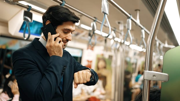 Professional caucasian project manager looking at watch while standing in train with blurred background. Professional business man calling to manager about investor surrounded by people. Exultant.