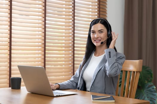 Female call center operator or customer service helpdesk staff working on workspace while talking on the headset to provide assistance for customer. Professional modern business service. Blithe