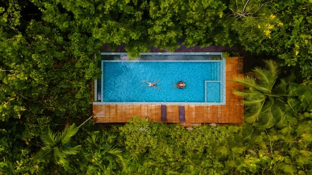 couple of men and women in a swimming pool in the jungle of Krabi Thailand, aerial view with a drone above a swimming pool in the jungle rainforest of Thailand.