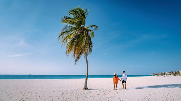 Eagle Beach Aruba, Palm Trees on the shoreline of Eagle Beach in Aruba, couple man, and woman on the beach of Aruba walking on the beach in the evening during vacation