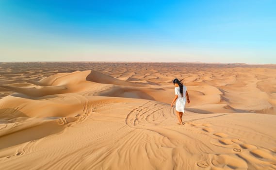 Dubai desert sand dunes, an Asian woman on Dubai desert safari, United Arab Emirates vacation, woman on vacation in Dubai walking at the sand dunes of Dubai