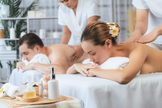 Caucasian couple customer enjoying relaxing anti-stress spa massage and pampering with beauty skin recreation leisure in day light ambient salon spa at luxury resort or hotel. Quiescent