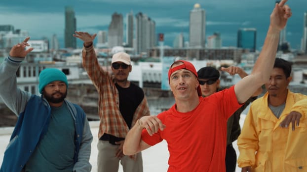 Multicultural teenagers dancing while looking at camera on rooftop with urban city view. Professional break dance group moving to hip-hop music with friends cheer. Outdoor sport 2024. Endeavor.