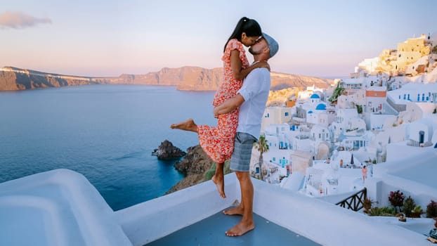 Santorini Greece, a young couple on luxury vacation at the Island Santorini watching the sunrise by the blue dome church and whitewashed village Oia Santorini during summer holidays