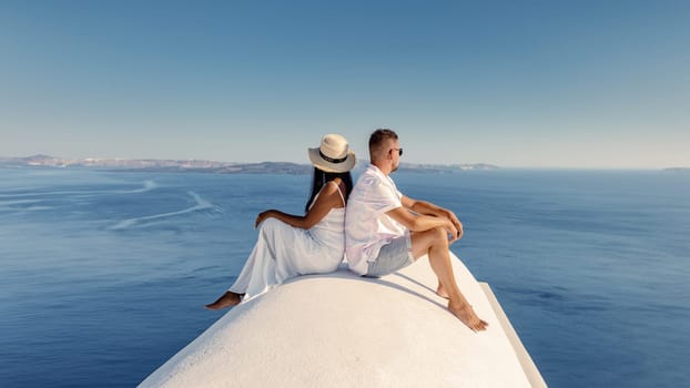 Santorini Greece, a young couple on a luxury vacation at the Island Santorini. men and woman sitting an a whitewashed dome by the ocean looking out over the caldera of Santorini