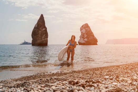 Close up shot of beautiful young caucasian woman with black hair and freckles looking at camera and smiling. Cute woman portrait in a pink bikini posing on a volcanic rock high above the sea