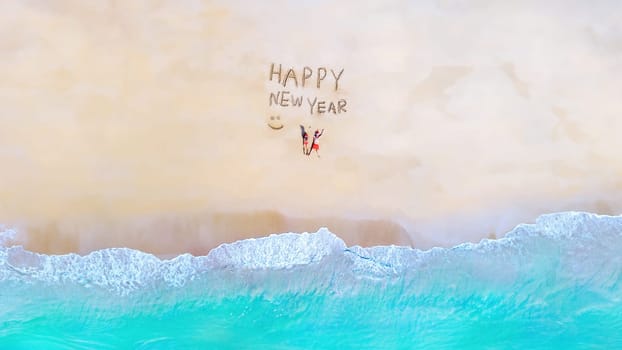 a couple on the beach with a Happy New Year sign, men and women lying down on the beach view from above with Happy New Year words written on the beach in Thailand