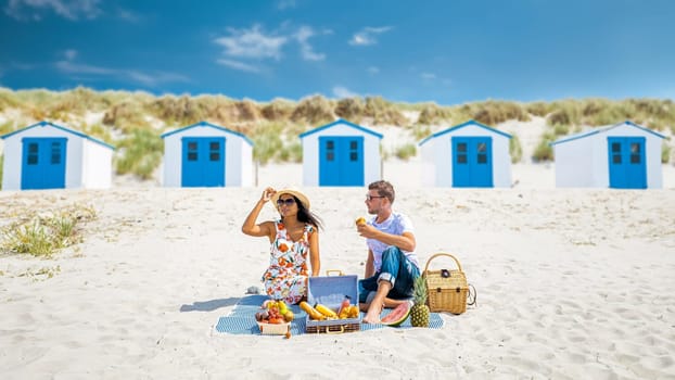 Picnic on the beach Texel Netherlands, couple of men and woman having a picnic on the coast of Texel with white sand and a colorful withe and blue house in Holland