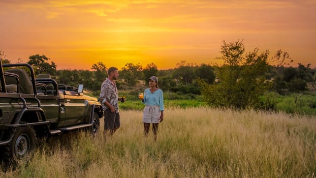 Asian women and European men on safari game drive in South Africa Kruger National Park. a couple of men and women on safari watching the sunset. Tourists looking sundowner with drinks on safari