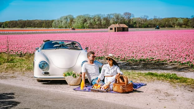 Lisse Netherlands a couple doing a road trip with an old vintage car in the Dutch flower bulb region with tulip fields during Spring