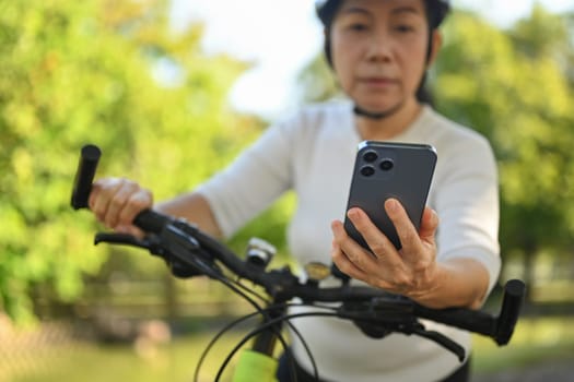 Senior woman hand using mobile phone checking route map location while riding exercise bicycle