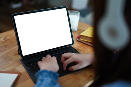 Closeup child girl hands typing on keyboard of digital tablet while doing homework at dinning table.