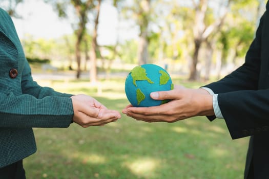 Earth day concept, businessman giving Earth globe to colleague as CSR corporate social responsible principle to promote environmental awareness and embrace ESG for greener and sustainable future. Gyre