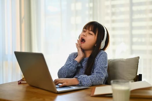 Little student girl yawning and bored while studying online at home