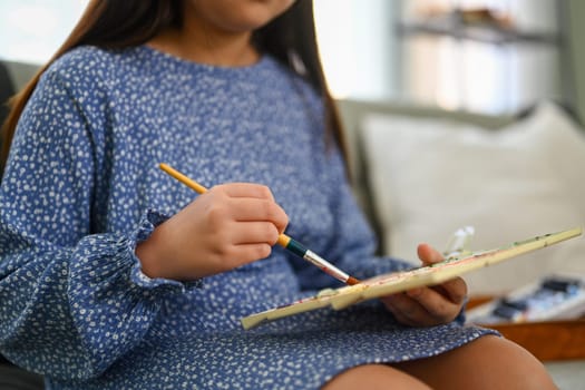 Cropped shot of little girl in casual dress painting picture, enjoying leisure weekend activity at home