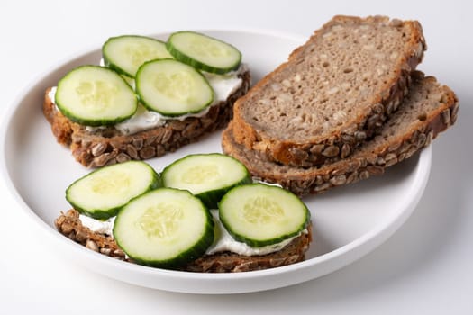 Rye bread with cream cheese and cucumbers on a white table. Whole grain rye bread with seeds.