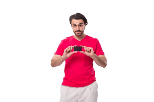 young brunette advertiser man dressed in a red t-shirt shows a plastic credit card.